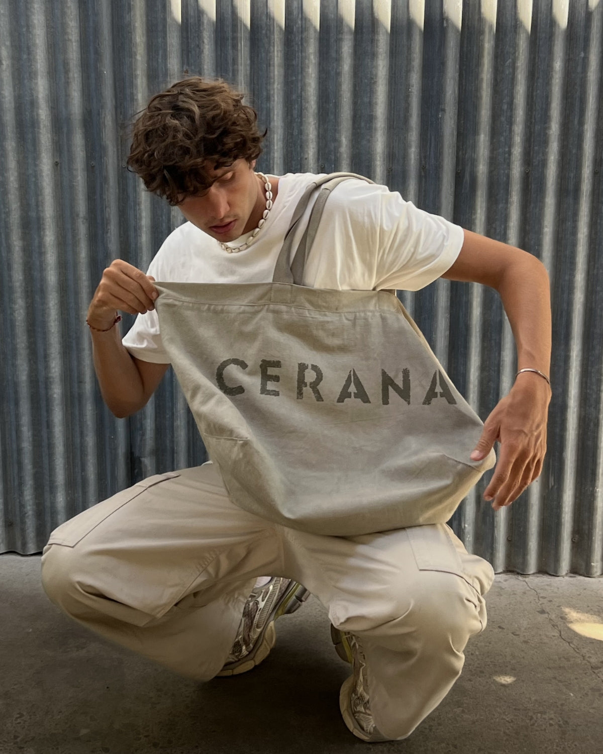 Person holding a beige bag with 'CERANA' branding against a corrugated metal background