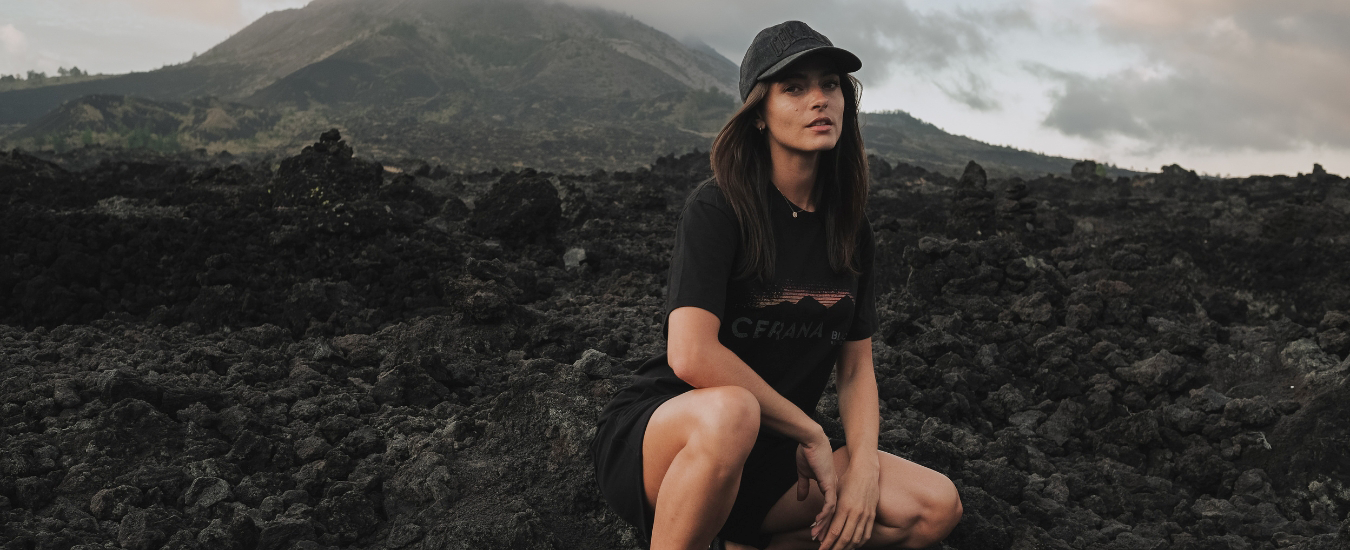 Girl Cerana Tshirt and Cap sitting on a rocky landscape with mountains in the background