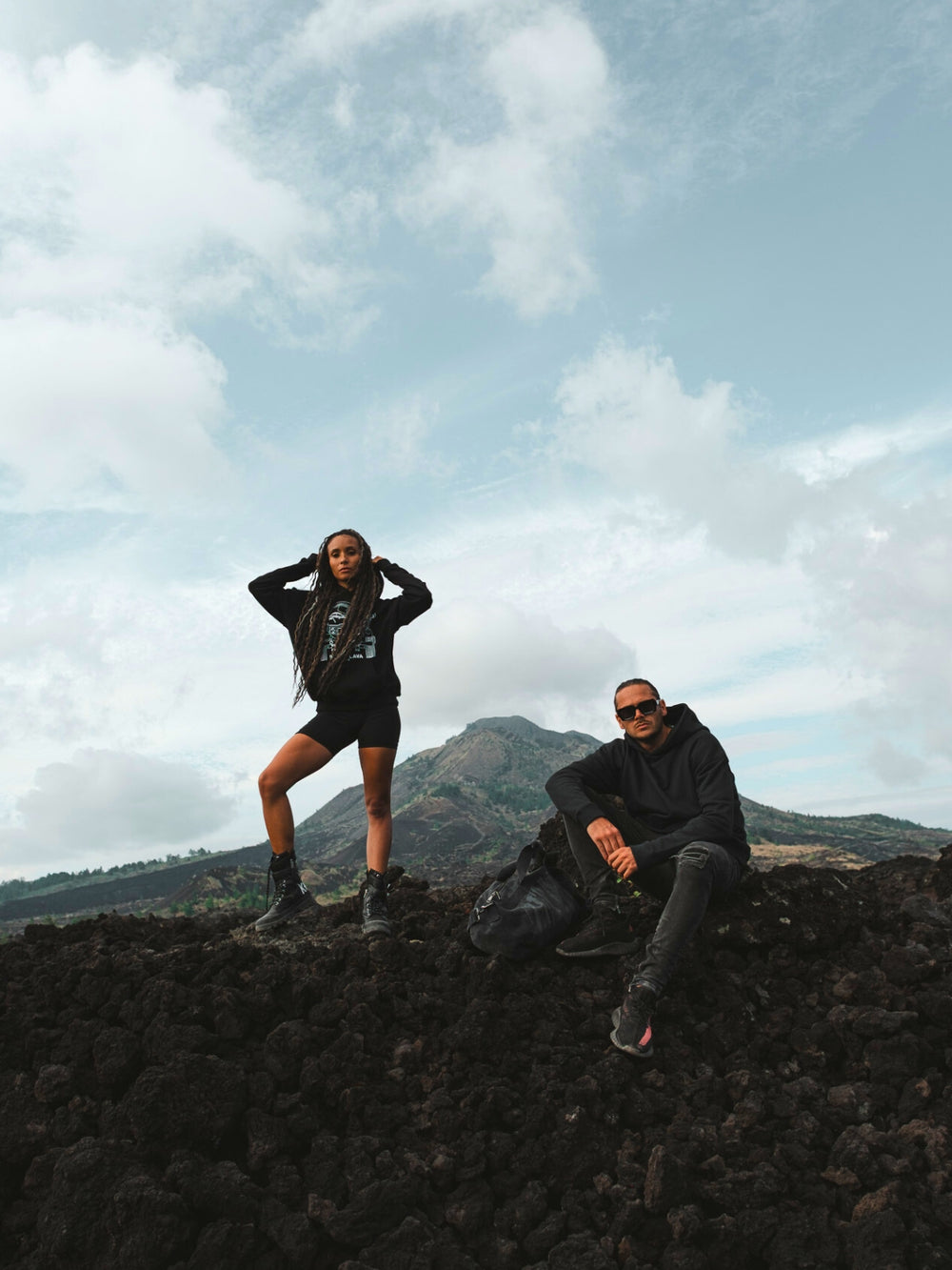 Cerana minimal black hoodie and duffle bag outfit captured in raw volcanic landscape – contemporary outdoor streetwear.