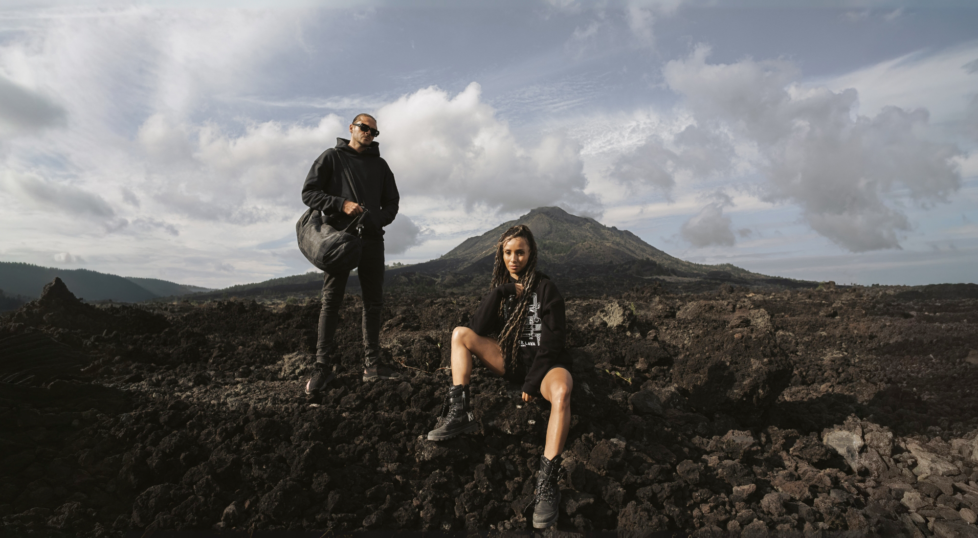 Cerana streetwear black hoodie and combat boots styled on volcanic landscape with mountain backdrop – rugged outdoor fashion look.