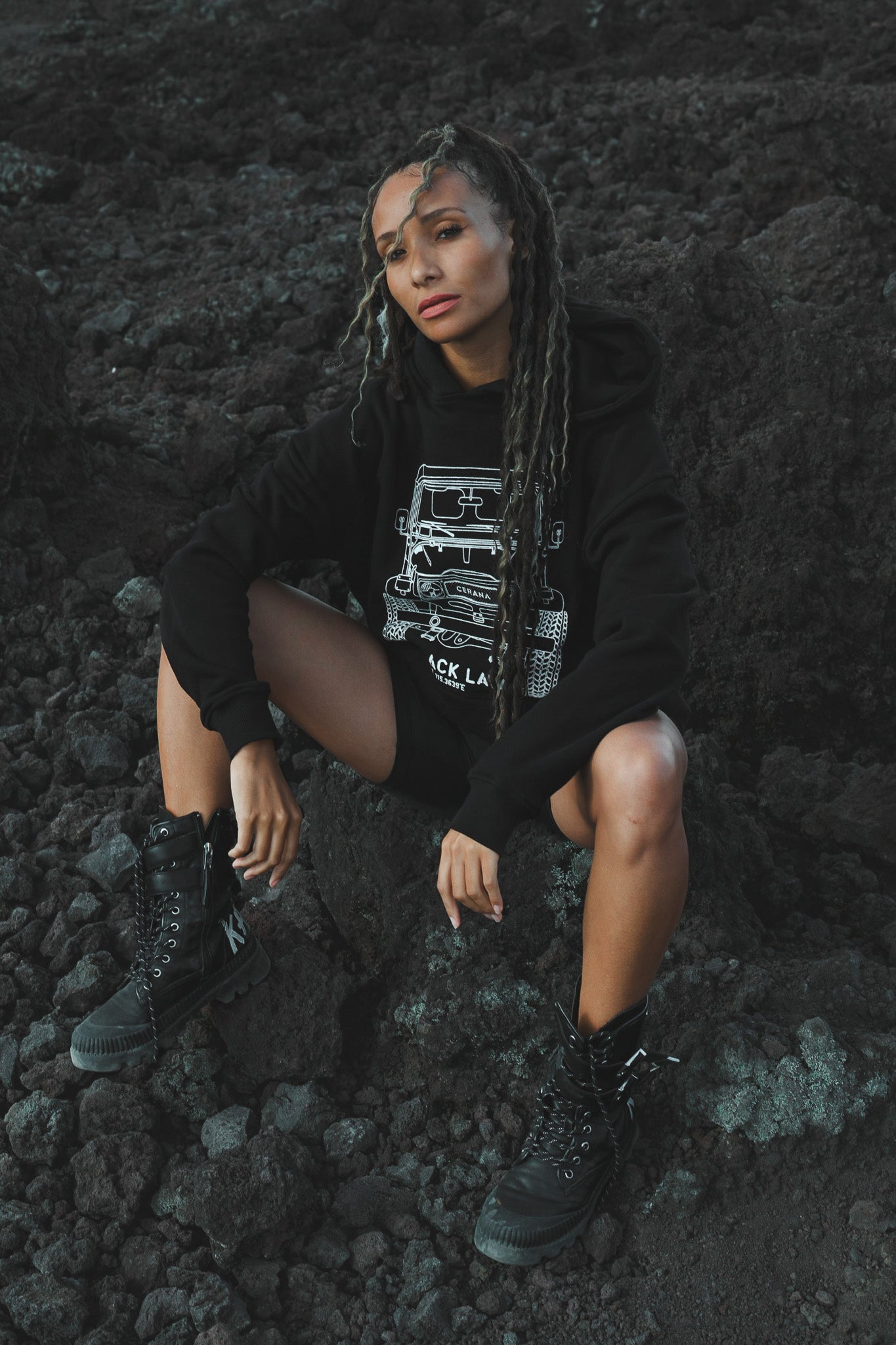 Cerana hoodie outfit featuring graphic print, styled with black lace-up boots on rocky volcanic backdrop – edgy streetwear vibe.